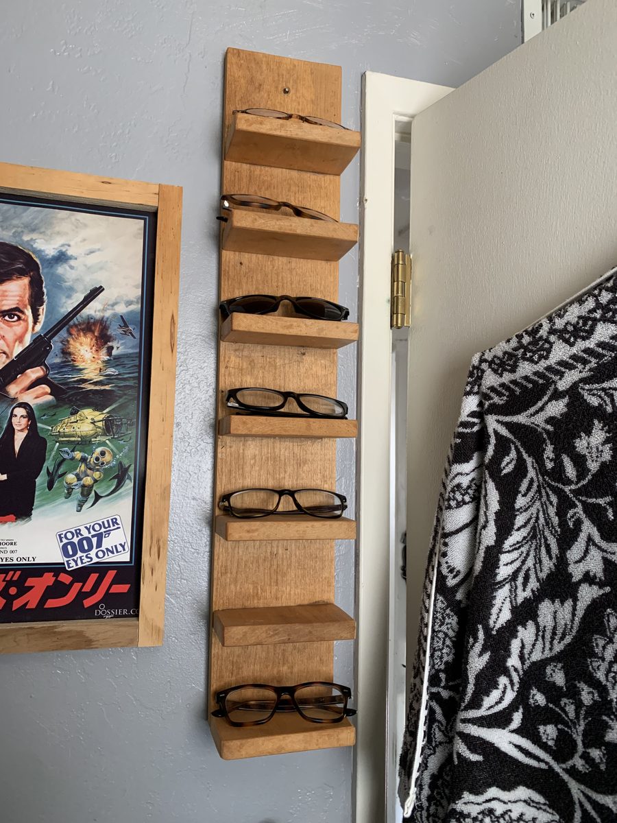 A wall-mounted wooden rack holding several pairs of glasses.